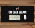 Black 16 x 32 inch desk mat that reads "On call again", on a wood desk with a keyboard and mouse below the joke