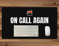 Black 24 x 14 inch desk mat that reads "On call again", on a wood desk with a keyboard and mouse below the joke