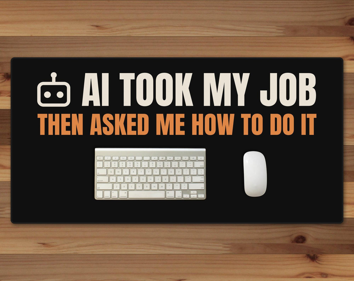 Black 16 x 32 inch desk mat that reads "AI took my job / Then asked me how to do it", on a wood desk with a keyboard and mouse below the joke