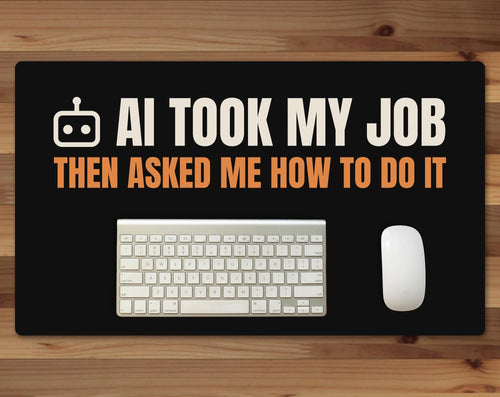 Black 24 x 14 inch desk mat that reads "AI took my job / Then asked me how to do it", on a wood desk with a keyboard and mouse below the joke