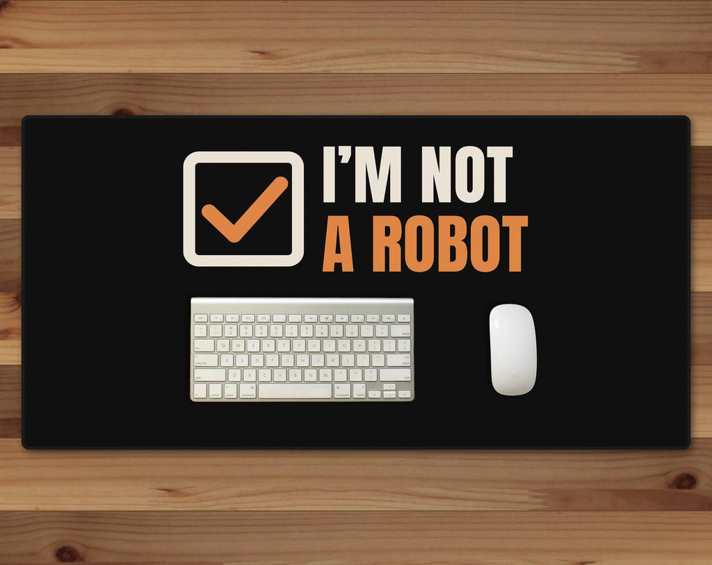 Black 16 x 32 inch desk mat that reads "I’m not / A robot", on a wood desk with a keyboard and mouse below the joke