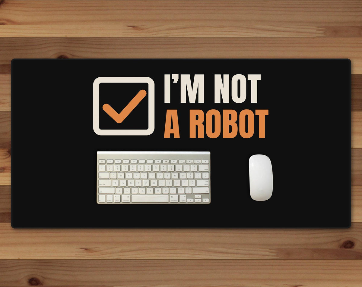 Black 16 x 32 inch desk mat that reads "I’m not / A robot", on a wood desk with a keyboard and mouse below the joke
