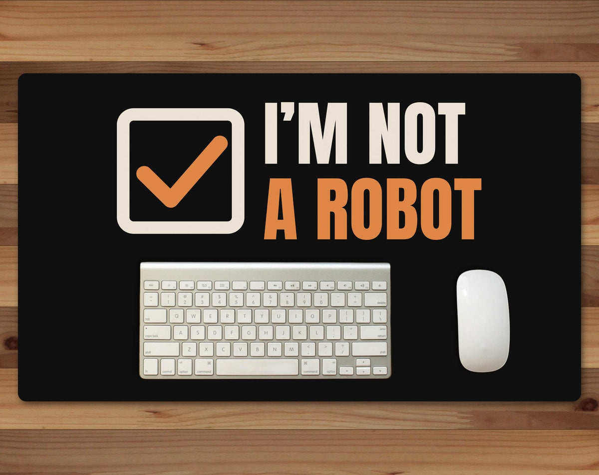 Black 24 x 14 inch desk mat that reads "I’m not / A robot", on a wood desk with a keyboard and mouse below the joke